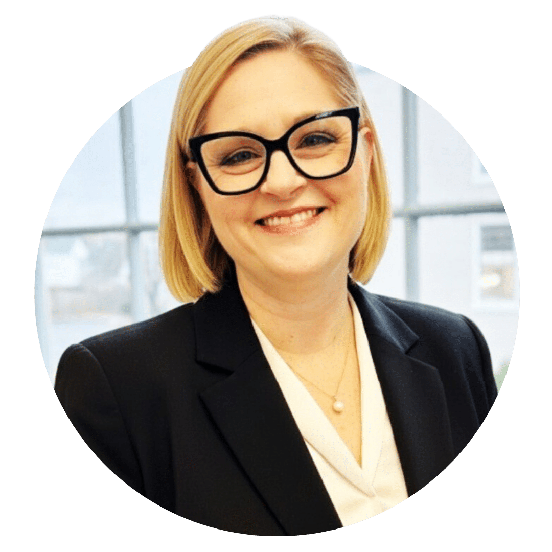 Smiling woman in glasses wearing a blazer in an office headshot
